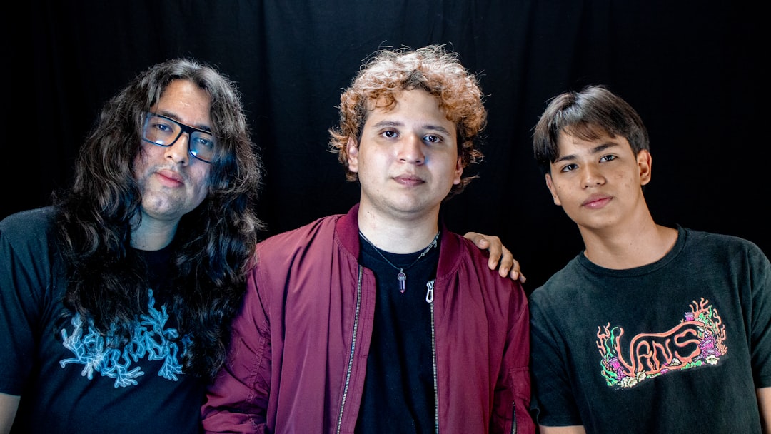 Three young men posing together against a dark background.